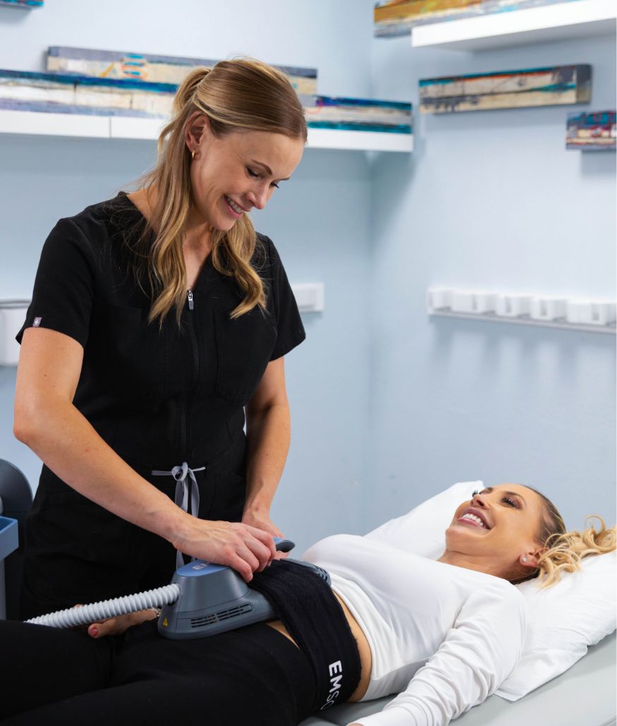 Clinician uses body contouring device on woman's abdomen in treatment room