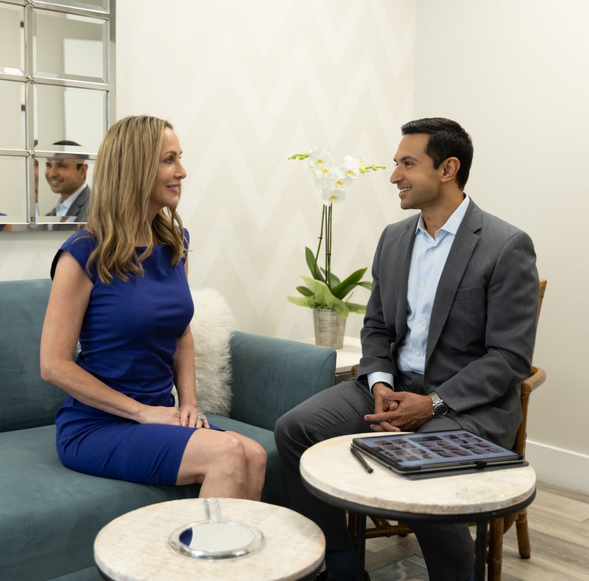 Woman in blue dress and doctor sit facing each other in a consultation room.